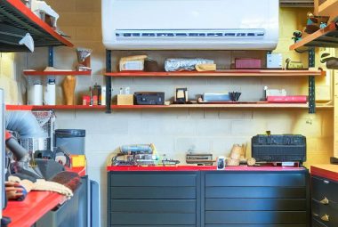 An image of visually appealing organized garage with a mini split system installed in a garage setting. The image showcases the indoor air handler mounted on the wall above a well-organized and comfortable garage environment, such as tools, storage boxes, or a workbench.
