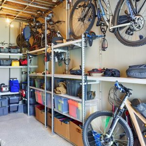 An image of a neat and well-organized garage or basement dedicated to outdoor gear storage. Visible in the image could be various types of gear, including bicycles hanging from wall mounts, camping equipment neatly arranged in labeled bins, a sturdy shelving system with items organized strategically according to frequency of use and weight, and a fishing rod rack in a corner.