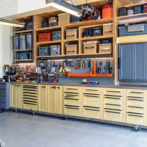 an image of a clean and organized garage and shows wooden cabinets and drawers as garage cabinet ideas including shelves that are stacked with neatly organized containers.