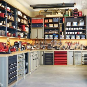 an image of an organized garage with shelving and a variety of garage cabinet ideas including a cabinet-workbench combo with tools.
